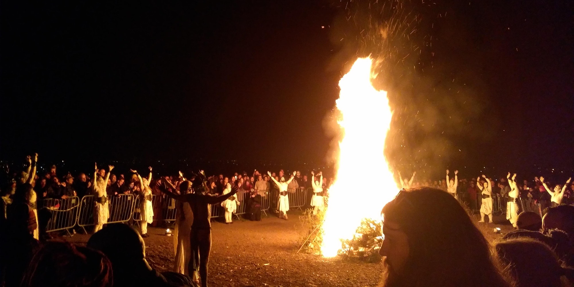 Bonfire at the Beltane Fire Festival 2019, Calton Hill, Edinburgh. The reunited May Queen and Green Man face the fire, while dancers stop to raise their arms to heaven. Photo by "Nyri0" This file is licensed under the Creative Commons Attribution-Share Alike 4.0 International license.